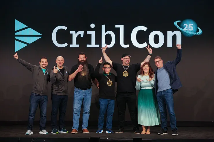 Paul Stout, in a cap and wearing a Cribl Community award medal, on stage at CriblCon 25 with the other award winners